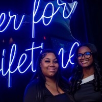 3 girls in front of Laker for a Lifetime neon sign